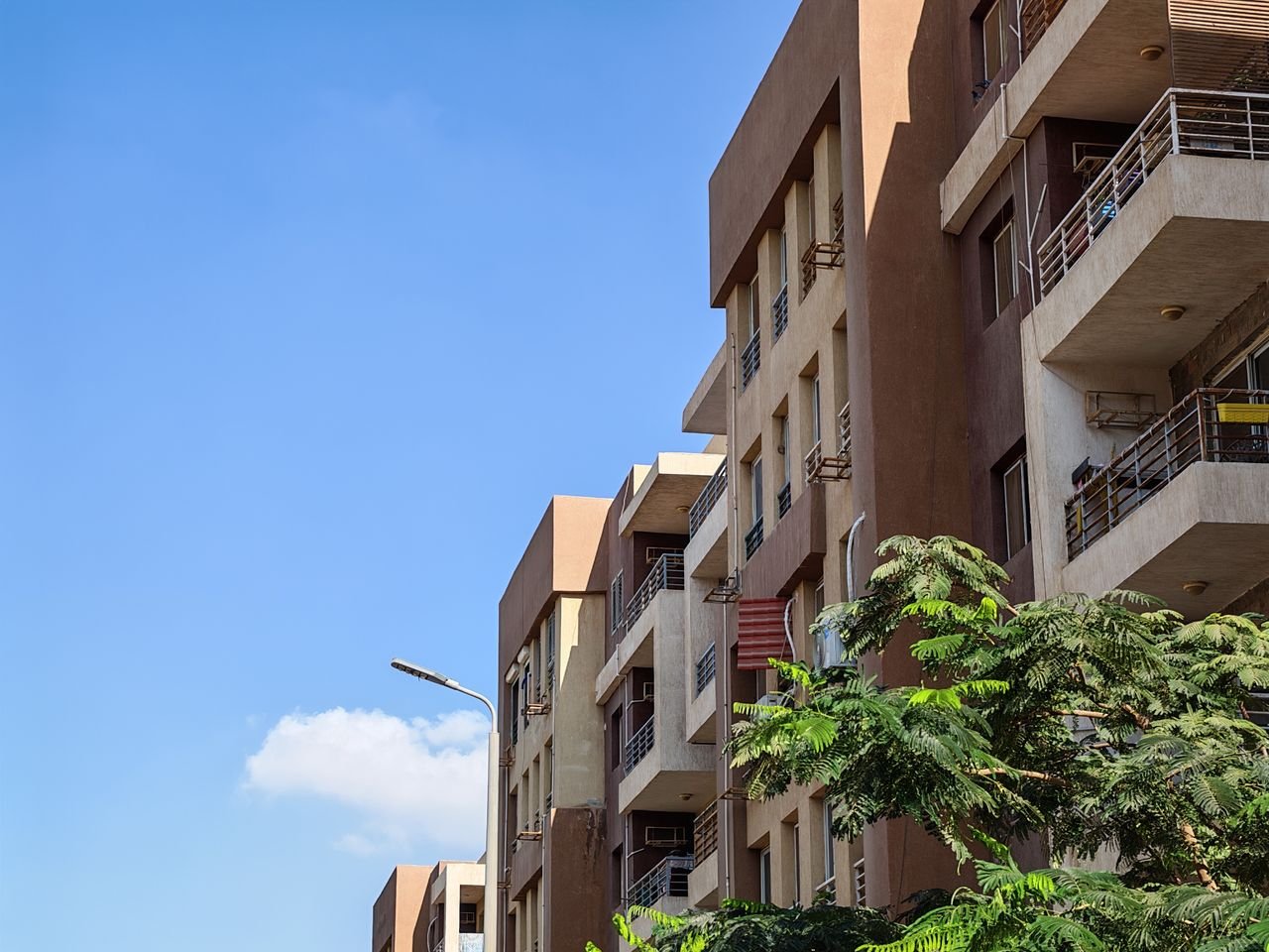why-choose-us Urban apartment building against a bright blue sky with foliage in the foreground.