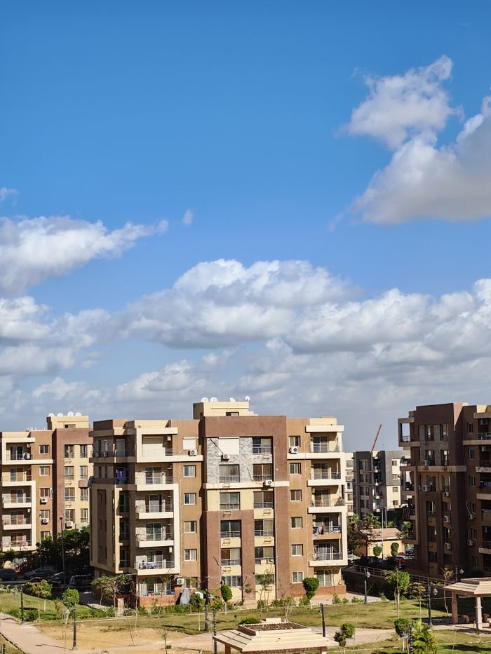 gallery-1 Contemporary apartment complex with bright blue sky and clouds.